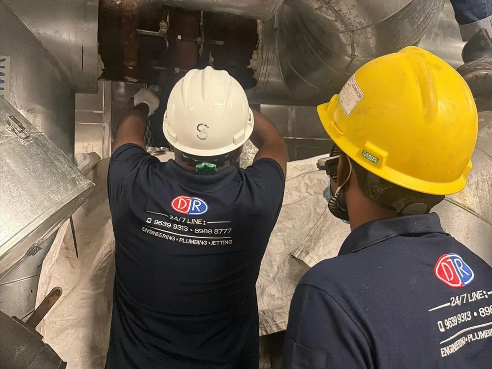 Two DJR plumbers in company uniforms and hard hats working on pipework in a plant room