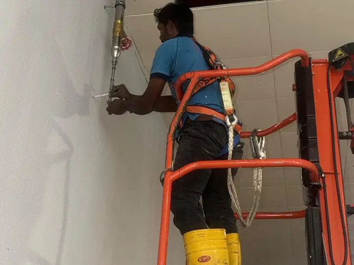 DJR technician in a safety harness repairing a pipe from a scissor lift