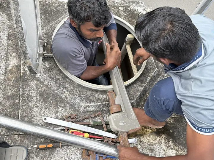 Two DJR plumbers fitting stainless steel pipe through a tank access hatch at an industrial site in Tuas