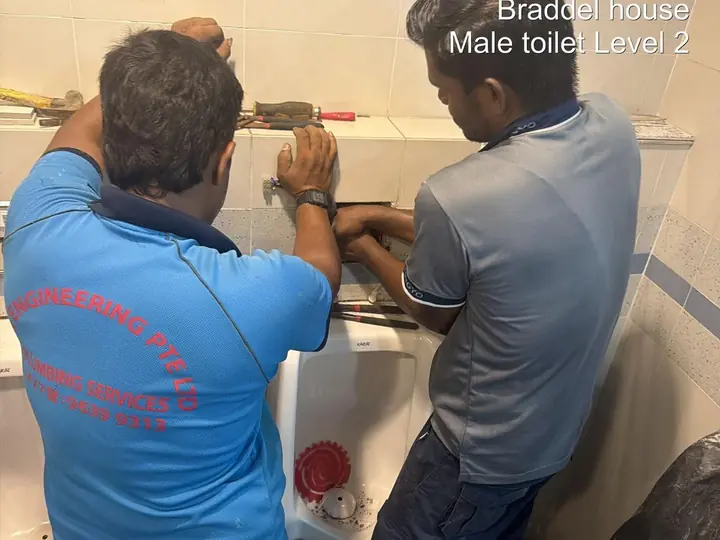 Two DJR plumbers replacing urinal pipework in an office building washroom in Toa Payoh